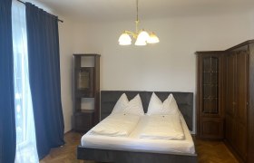 Schlafzimmer mit Doppelbett, dunklen Vorh&auml;ngen und Holzschr&auml;nken.