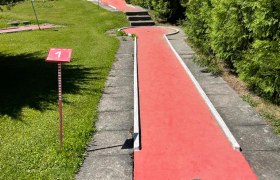 Minigolfbahn mit rotem Belag und gr&uuml;ner Hecke.