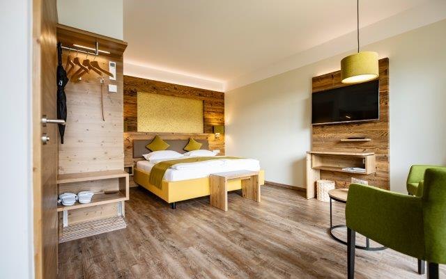 Modernes Hotelzimmer mit Holzmöbeln, Doppelbett, grünem Sessel und Flachbildfernseher.
