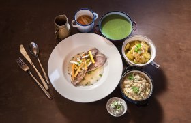 Tafelspitz in einem weißen Teller. Klassische Beilagen in kleinen Schälchen rund um den Teller gruppiert.