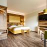 Modernes Hotelzimmer mit Holzm&ouml;beln, Doppelbett, gr&uuml;nem Sessel und Flachbildfernseher.