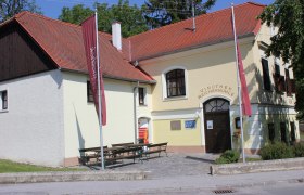 Gebäude mit gelber Fassade und roten Dachziegeln. Über dem Eingang steht "Vinothek Reichermühl"e