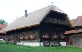 Traditionelles Holzhaus mit Strohdach und Blumenkästen im Freilichtmuseum Vorau.
