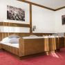Ein Schlafzimmer mit einem h&ouml;lzernen Doppelbett, rotem Teppichboden und zwei schwarz-wei&szlig;en Bildern an der Wand.