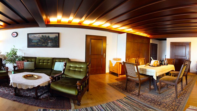 Hangulatos nappali fab&uacute;torokkal, z&ouml;ld kanap&eacute;val, &eacute;tkezőasztallal &eacute;s szőnyegekkel.