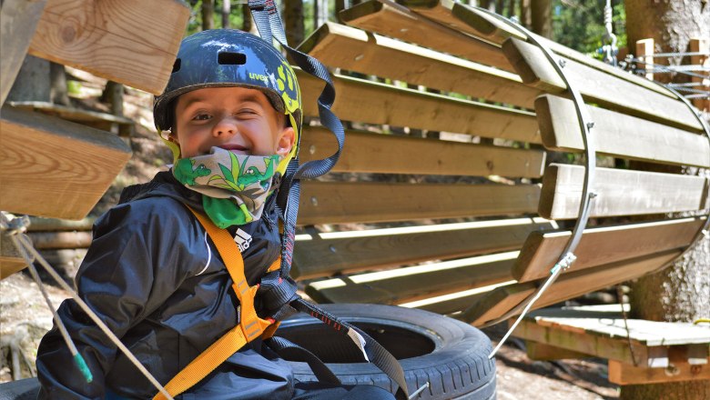 Ein Kind mit Helm und Sicherheitsgurt in einem Kletterpark.