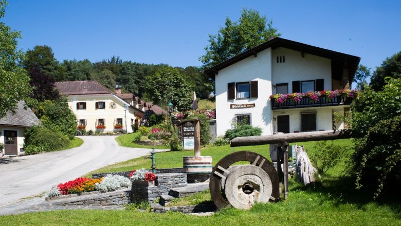 Ein ländliches Gästehaus mit Blumen und einem alten Mühlstein im Vordergrund.