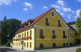 Mehrst&ouml;ckiges gelbes Geb&auml;ude mit roten Dachziegeln und Blumenk&auml;sten an den Fenstern.
