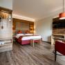 Modernes Hotelzimmer mit Doppelbett, Holzm&ouml;beln und rotem Sessel.