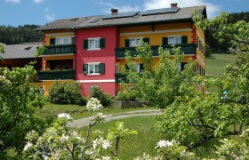 Ein Gebäude mit gelber und roter Fassade, umgeben von blühenden Bäumen und grünem Gras.