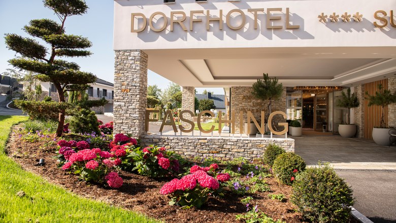 Eingang des Dorfhotels Fasching mit Blumenbeet und moderner Architektur.