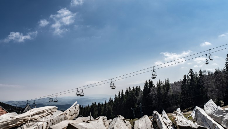 Blick auf eine Seilbahn über einem Wald mit blauem Himmel im Hintergrund.