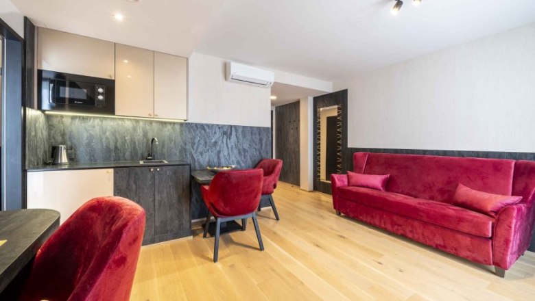 Modernes Apartment mit rotem Sofa und St&uuml;hlen, kleiner K&uuml;che und Holzboden.