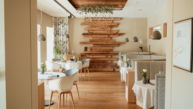 Innenansicht eines eleganten Restaurants mit Holzboden, modernen M&ouml;beln und dekorativen Holzelementen an der Wand.