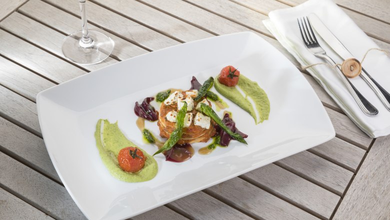 Gourmetgericht auf weißem Teller mit Gemüse und Soßen, daneben ein Glas Weißwein.