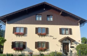 Ein traditionelles zweist&ouml;ckiges Haus mit Holzverkleidung und Blumenk&auml;sten vor den Fenstern.