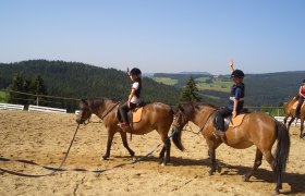 Kinder reiten auf Ponys in einer l&auml;ndlichen Umgebung mit H&uuml;geln im Hintergrund.