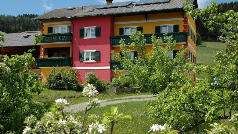 Ein Gebäude mit gelber und roter Fassade, umgeben von blühenden Bäumen und grünem Gras.