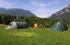 Zwei gr&uuml;ne Zelte auf einer Wiese mit Bergen im Hintergrund.