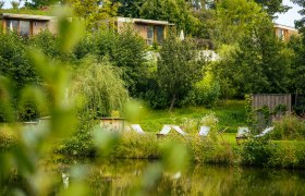 Ein ruhiger Garten mit Liegestühlen am Teich, umgeben von Bäumen und grüner Vegetation.