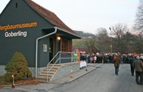 Au&szlig;enansicht eines Holzgeb&auml;udes mit einer Menschenmenge davor.