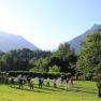 Gruppe von Menschen macht Tai Chi auf einer Wiese vor Bergkulisse.