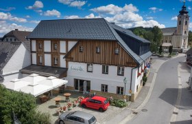 Luftaufnahme eines Gasthauses mit Terrasse, daneben eine Kirche.