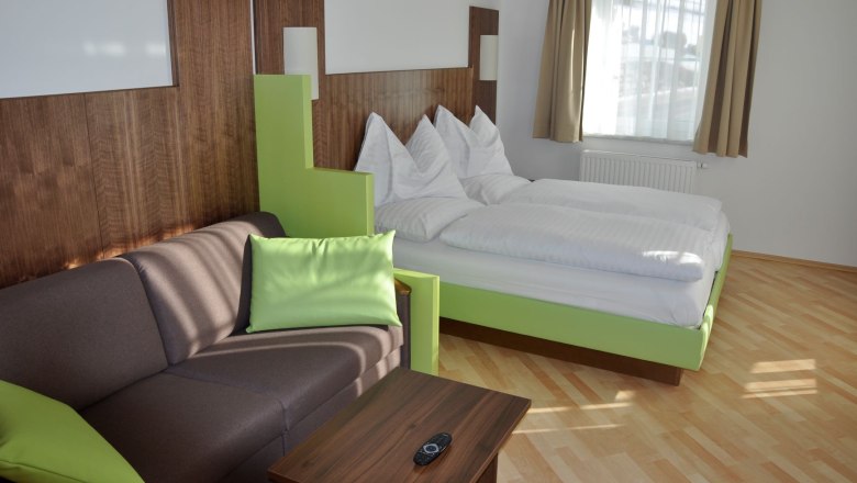 Modern eingerichtetes Hotelzimmer mit Doppelbett, Sofa und Holztisch.
