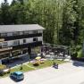 Au&szlig;enansicht des Gasthofs Berghof mit Terrasse und Parkplatz, umgeben von B&auml;umen.