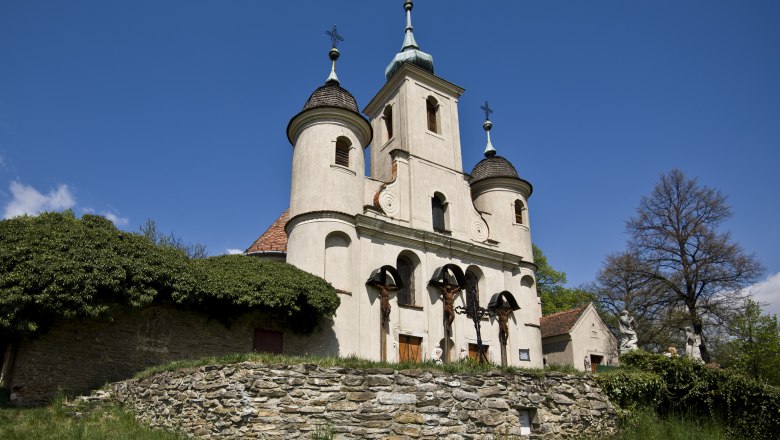 Historische Kirche mit drei Türmen und Kreuzigungsdarstellung, auf einem Hügel gelegen.