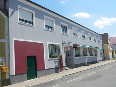 Zweistöckiges Gebäude mit grauer Fassade und mehreren Fenstern an einer Straße.