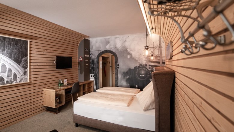 Hotelzimmer mit Holzw&auml;nden, einem Doppelbett und einem gro&szlig;en Wandbild einer Dampflok.
