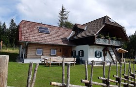 Eine gemauert Hütte, umgeben von grüner Wiese und einem Holzzaun.