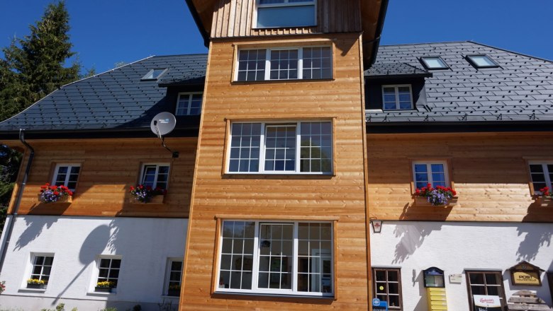 Alpengasthof Schanz, © Tourismusverband Oststeiermark, Sarah Schweiger Fassade eines Alpengasthofs mit Holzverkleidung und Blumenkästen unter blauem Himmel.
