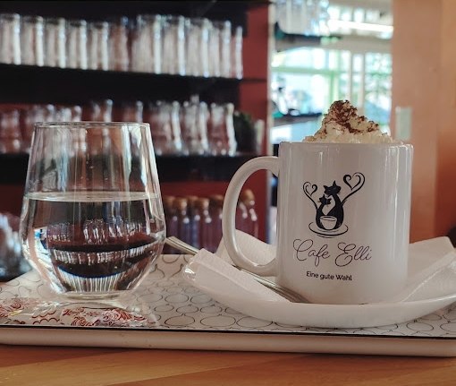 Ein Tablett mit einem Glas Wasser und einer Tasse mit einem Hei&szlig;getr&auml;nk mit Schlagobers im Cafe Elli.