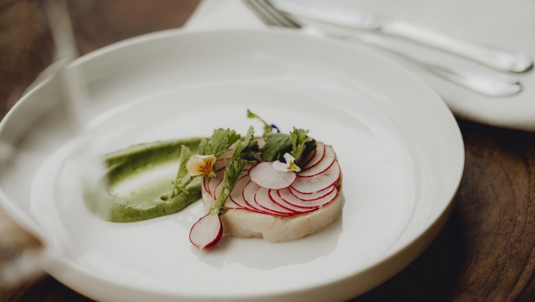 Ein Tellergericht mit Saibling, Radieschen und Wasabi-Creme, dekoriert mit essbaren Bl&uuml;ten.