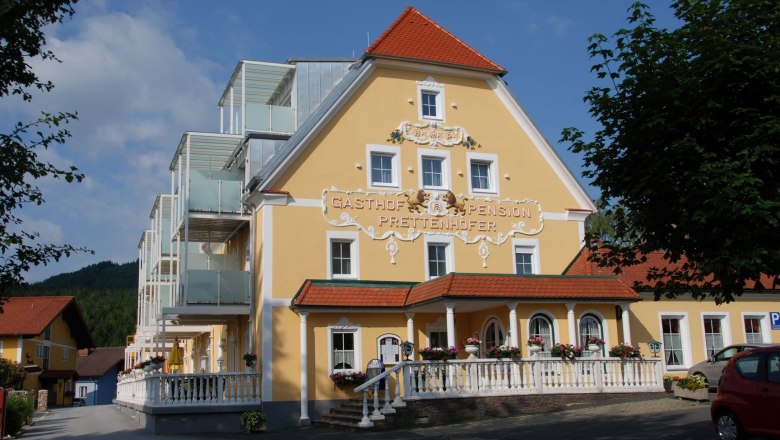 Joglland Hotel Prettenhofer, © Joglland Hotel Prettenhofer Gelbes Hotelgebäude mit rotem Dach und modernen Balkonen.