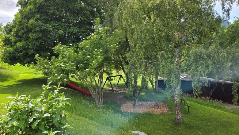 Ein gr&uuml;ner Garten mit B&auml;umen, einer Schaukel und einer Rutsche.