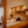 Gem&uuml;tliches Appartement mit Doppelbett und Balkont&uuml;r. Die Wand ist zum Teil mit hellem Holz verkleidet, hinter dem Bett ist eine in die Wand eingelassene Nische mit Ablagefl&auml;che und Spots, in einem erdigen Gold gestrichen.
