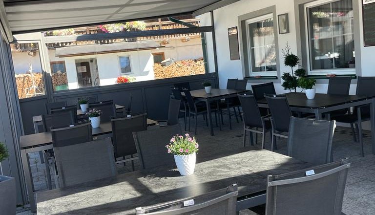 Überdachte Terrasse mit Tischen und Stühlen, dekoriert mit Blumen.
