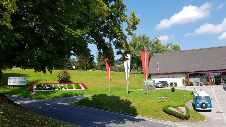 Eingangsbereich mit grünem Rasen, Blumenbeet und einem blauen Oldtimer-Bus.