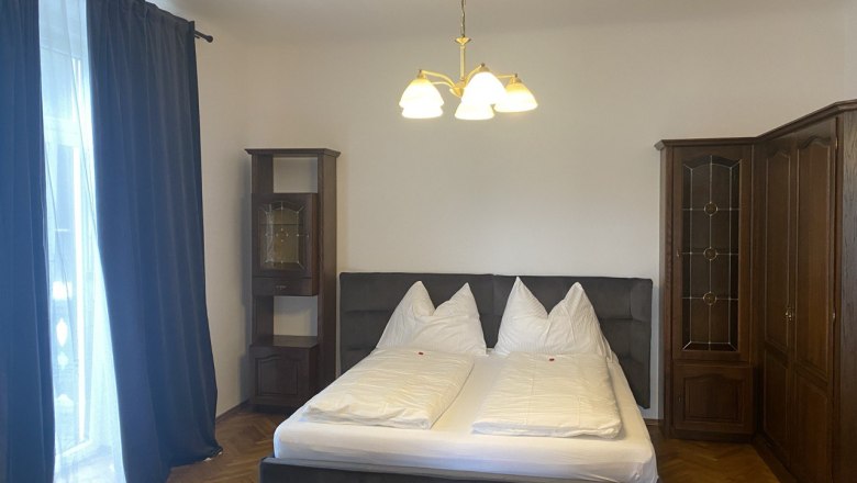 Schlafzimmer mit Doppelbett, dunklen Vorh&auml;ngen und Holzschr&auml;nken.