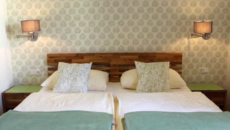 Gem&uuml;tliches Zimmer mit Doppelbett, Mustertapete, Wandlampen, Nachttischen und Kissen.